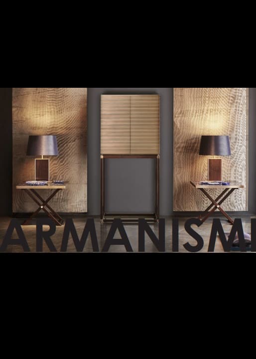 A graphic composition showing a room with two large decorative wall panels, imitating wood with a wavy grain. In the center, a wooden cabinet with a horizontal texture. On either side, two X-shaped side tables support two table lamps with dark blue lampshades. The text "ARMANISM" is in the lower foreground, with the letters cut out from the background.